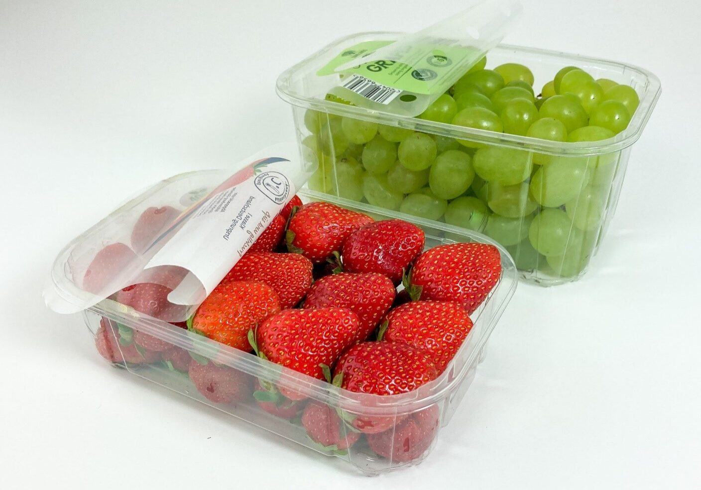 Two containers of strawberries and grapes on a table.
